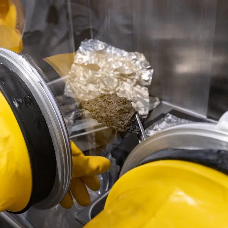 person inspects moon rock in a clear box with yellow rubber gloves