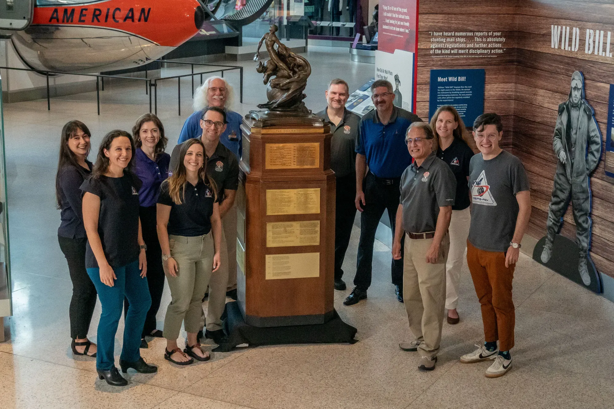 team stands next to Robert J. Collier trophy in the Smithsonian's National Air and Space Museum in Washington