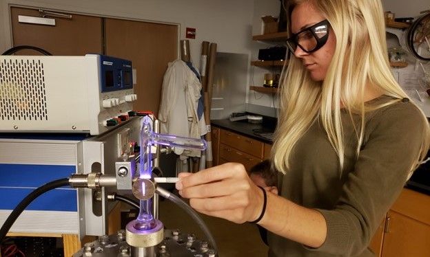 A woman twists a knob coming off of a glowing purple glass tube.